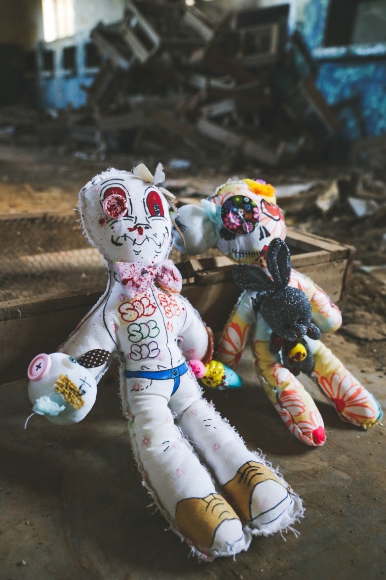 Close-up of two embroidered fabric dolls sitting in the ruins