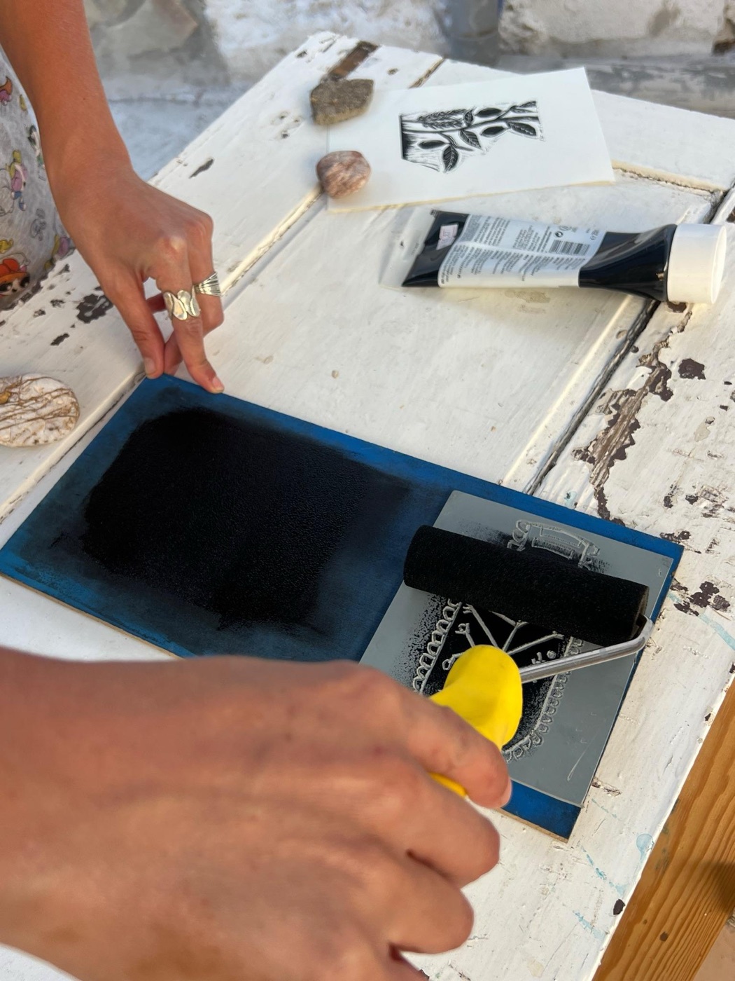 Hands inking a printing block with a roller on a weathered table