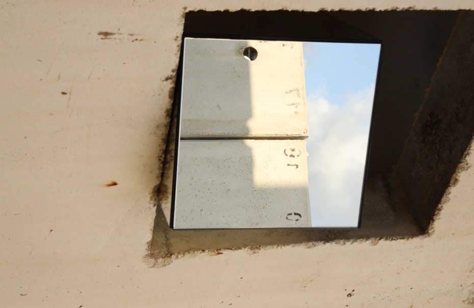 A mirror set into a concrete wall opening, reflecting the sky